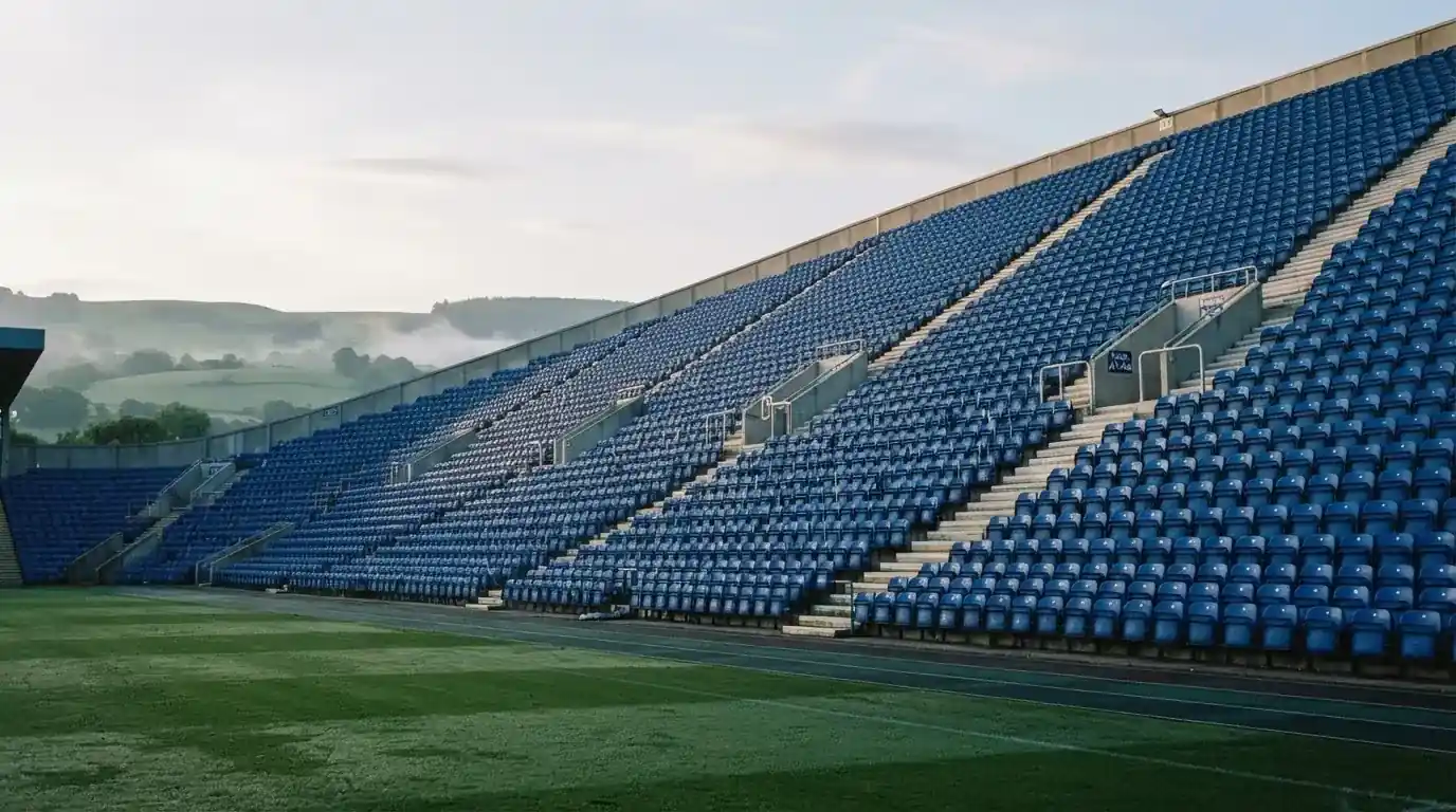 Ein leeres Stadion im Morgenlicht mit Blick auf die Sitzreihen, im Hintergrund Hügel und aufsteigender Nebel.