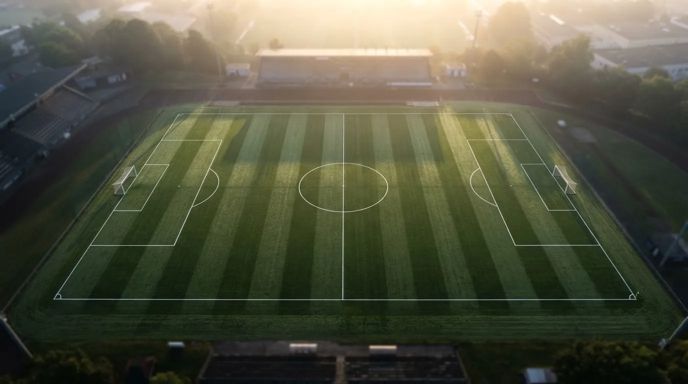 Ein Fussballplatz von oben gesehen, die Linien bilden ein helles Muster auf dem Rasen, Drohnenperspektive in der Morgendämmerung.