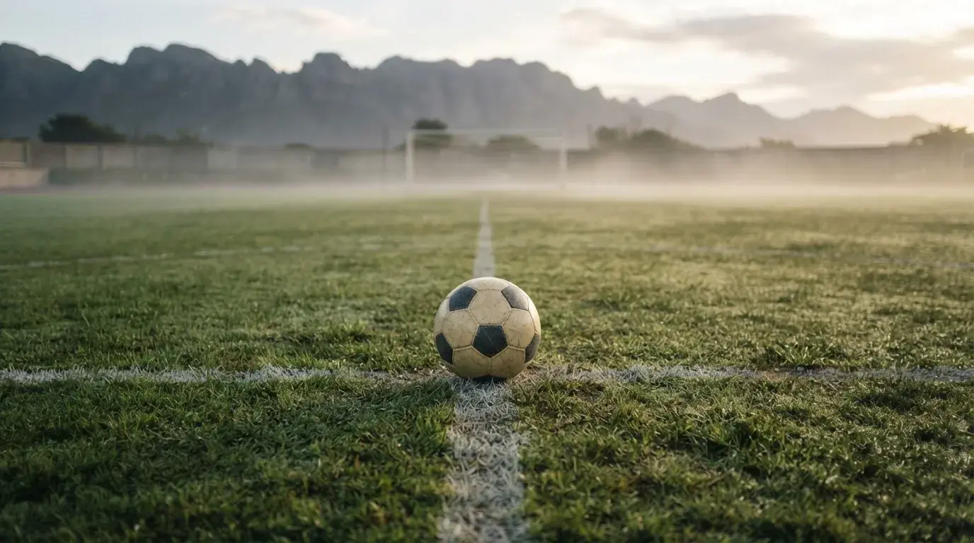 Ein einzelner Fussball auf dem Mittelpunkt eines leeren Rasens im Morgennebel, hinter dem Tor ragen Berge auf