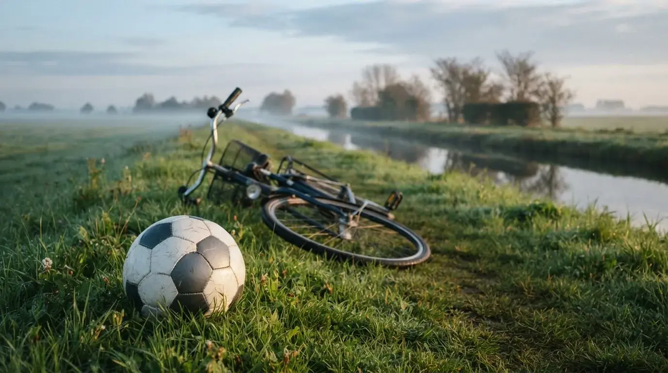 Ein Fussball liegt auf einer Wiese neben einem Fahrrad, im Hintergrund ein Kanal im Morgenlicht